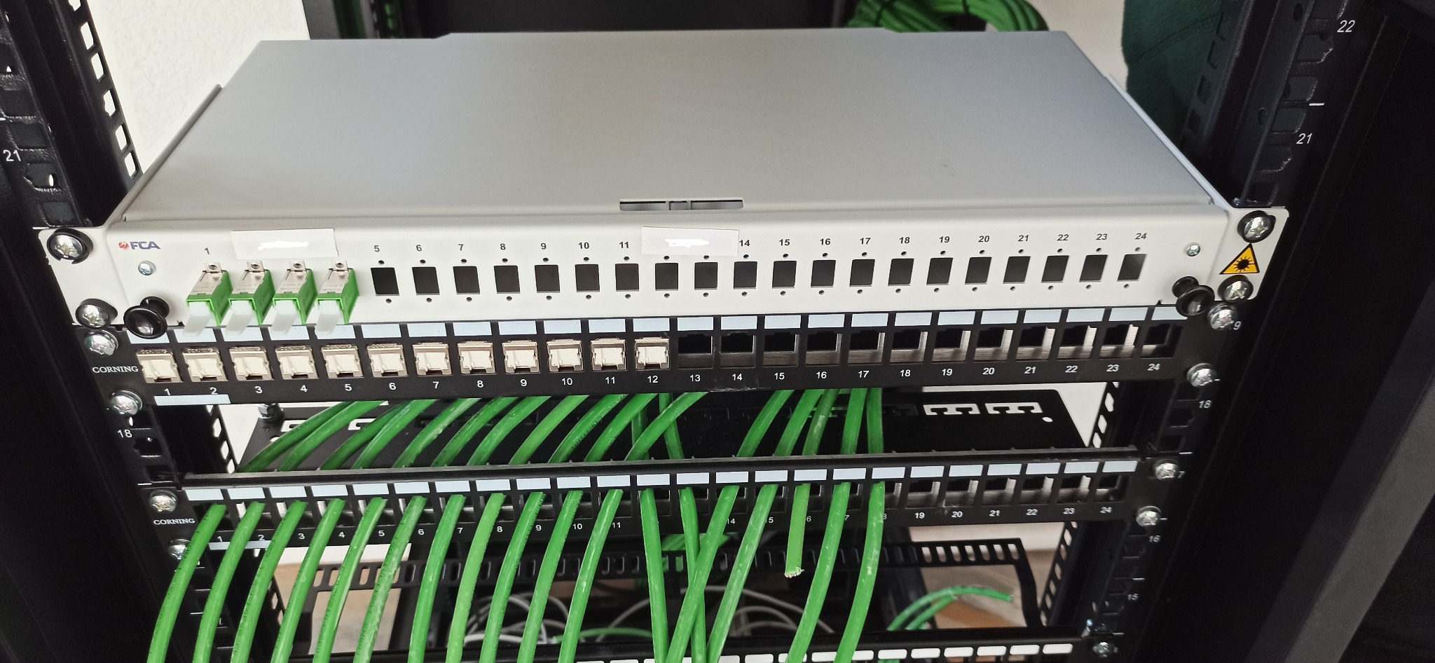 Panel krosowniczy z podłączonymi kablami światłowodowymi i miedzianymi w szafie rack, widoczne oznaczenia portów i logo producenta FCA.