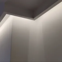 Świeżo pomalowane ściany z ukrytym oświetleniem LED na suficie, widoczne surowe wykończenie ościeżnicy drzwiowej w trakcie remontu.