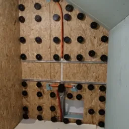 Poddasze w trakcie adaptacji na łazienkę: widoczne płyty OSB z mocowaniami instalacji, rury instalacyjne i fragment ściany pokrytej płytą gipsowo-kartonową.