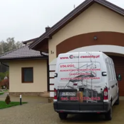 Biały samochód dostawczy Renault Master z reklamą firmy remontowej na tle domu jednorodzinnego z beżową elewacją i brązowymi akcentami.