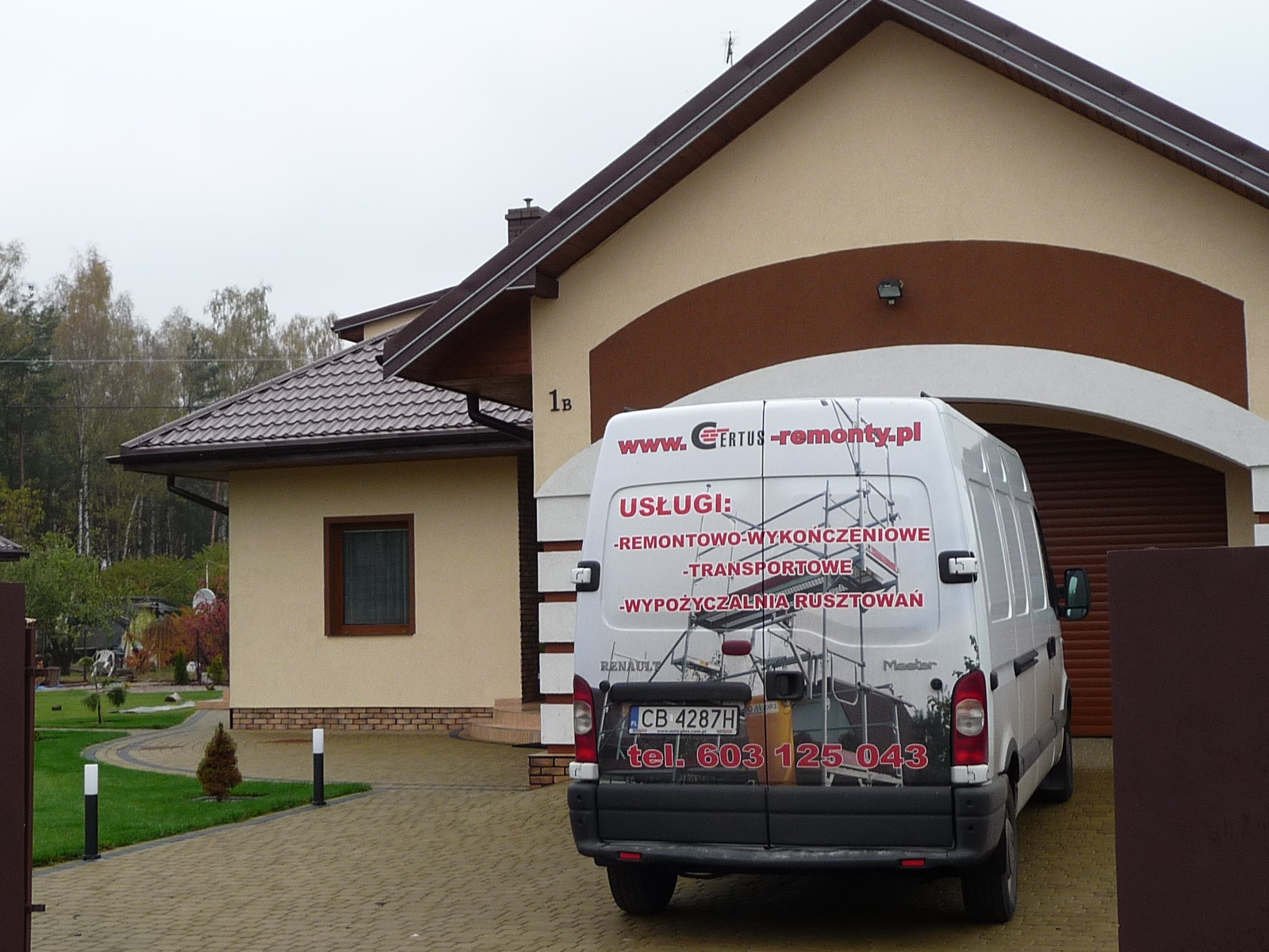 Biały samochód dostawczy Renault Master z reklamą firmy remontowej na tle domu jednorodzinnego z beżową elewacją i brązowymi akcentami.