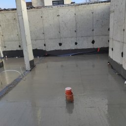 Andrii Vuichyk - Świeżo wylana betonowa posadzka wewnątrz budynku z surowymi, betonowymi ścianami i zaizolowanymi fundamentami, widoczne rury wentylacyjne i elementy szalunku.