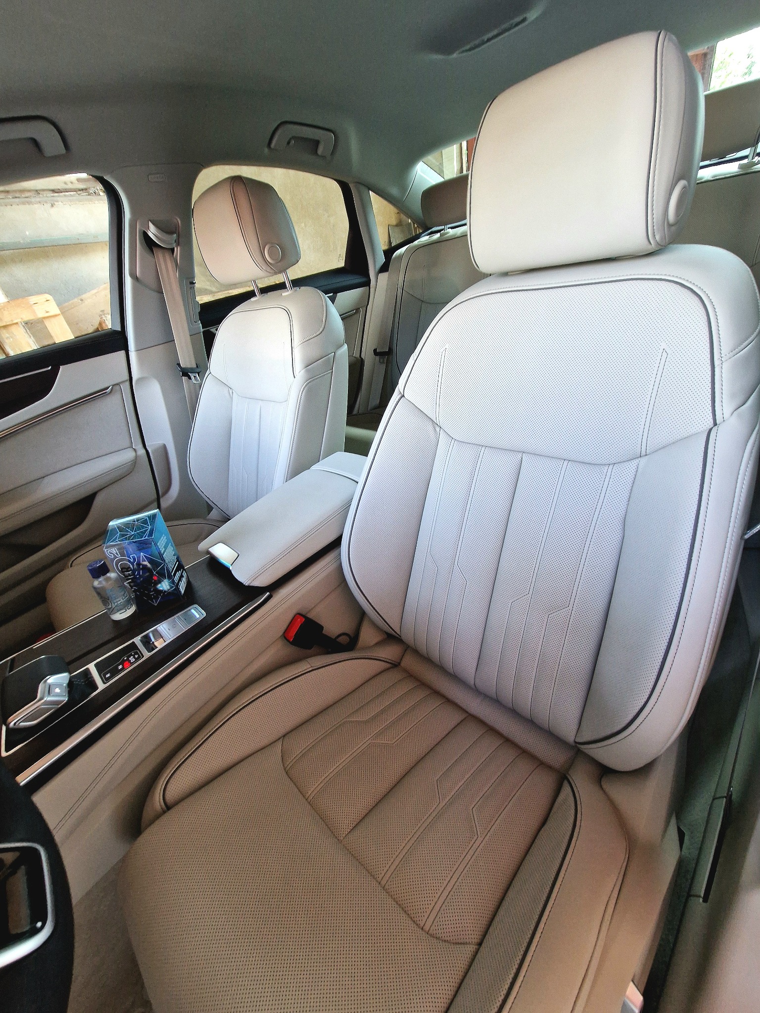 Jasna, perforowana skórzana tapicerka samochodowa po czyszczeniu, widoczne detale szwów i boczne panele drzwi, butelka wody i pudełko na konsoli środkowej.