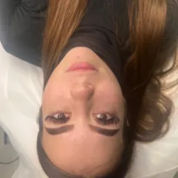 Kobieta leżąca na białym podłożu z widocznymi, przedłużonymi rzęsami i delikatnym makijażem ust.