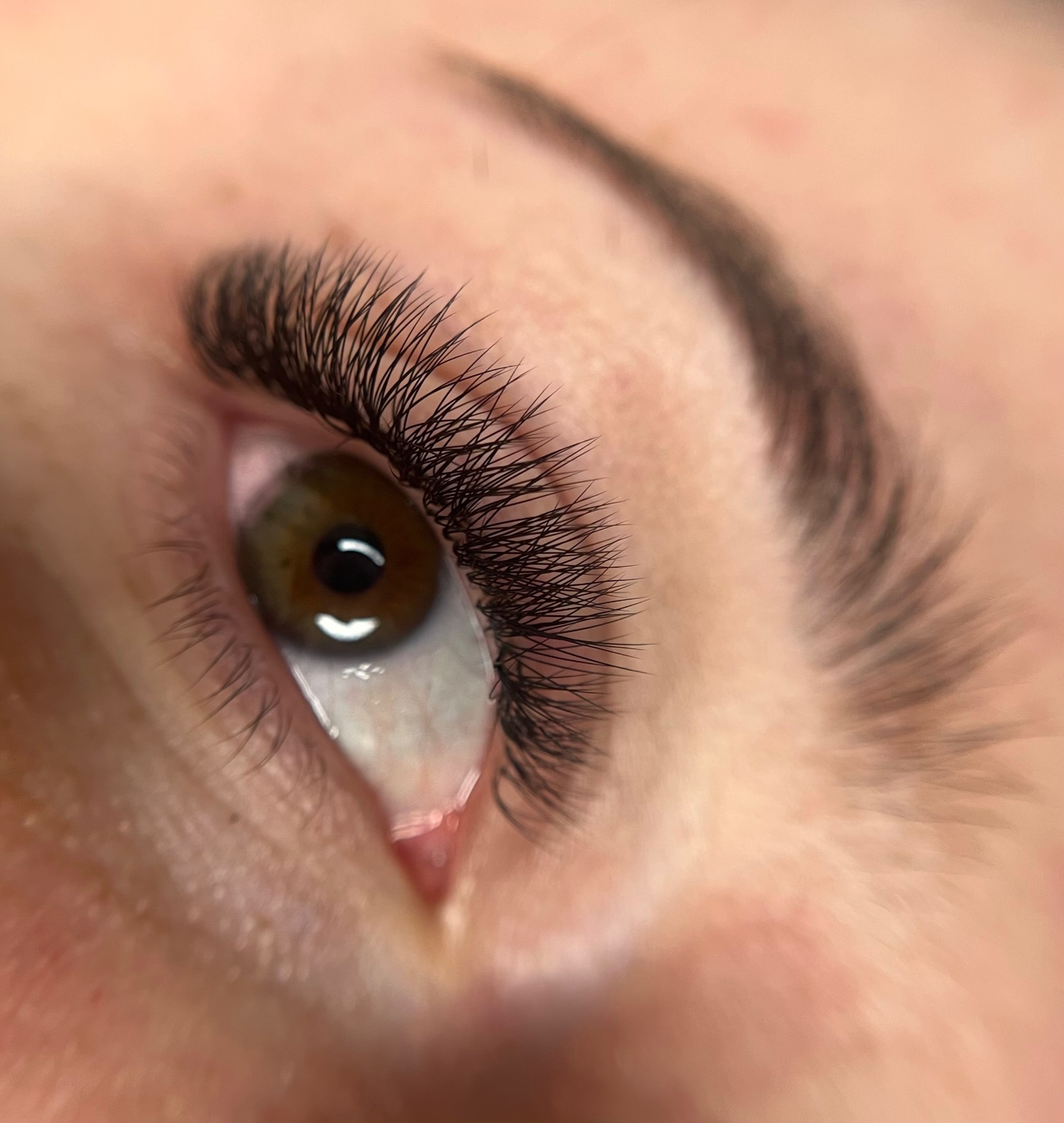 Zbliżenie na oko z przedłużonymi, gęstymi, czarnymi rzęsami; widoczna brązowa tęczówka z odbiciem światła i delikatnie zarysowany łuk brwiowy.