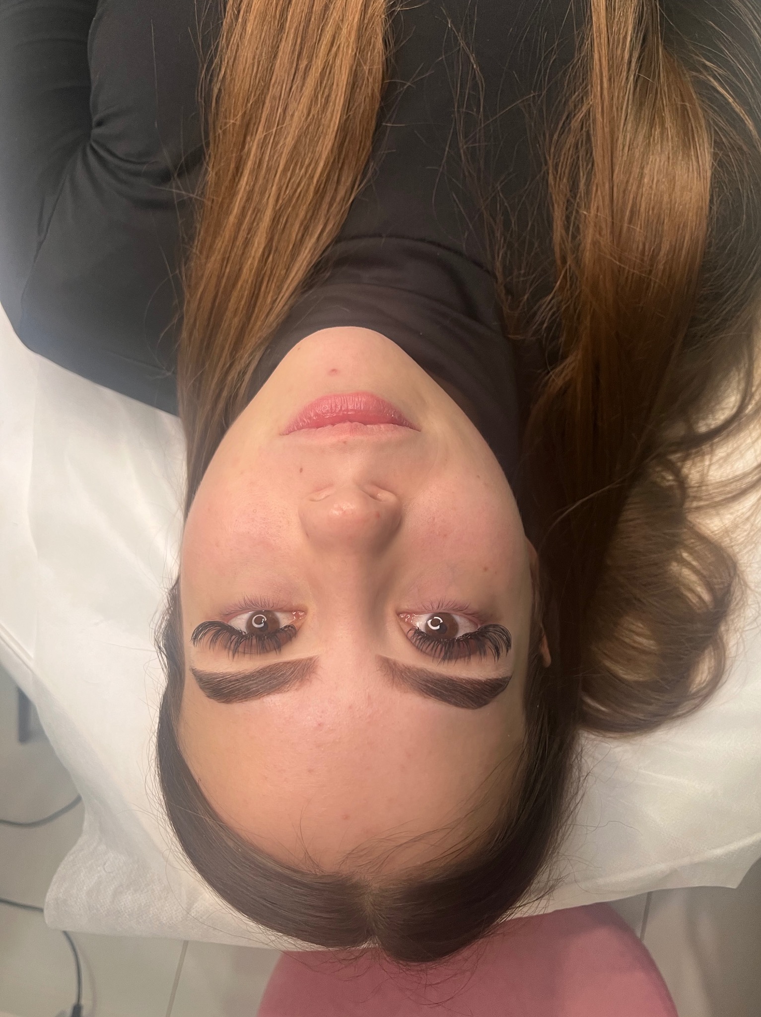 Kobieta leżąca na białym podłożu z widocznymi, przedłużonymi rzęsami i delikatnym makijażem ust.