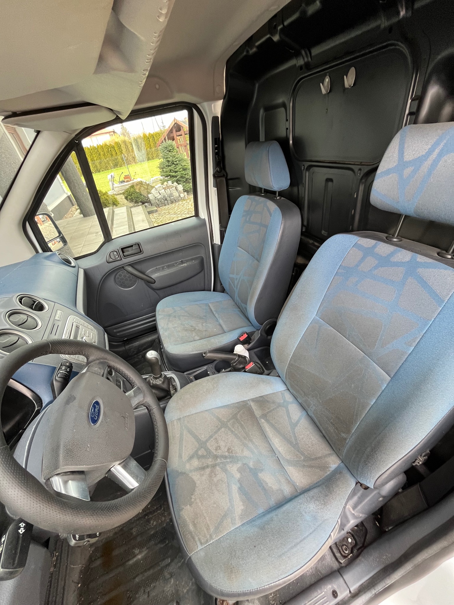 Wnętrze samochodu dostawczego Ford Transit Connect z brudnymi, niebiesko-szarymi fotelami z geometrycznym wzorem, widoczne z perspektywy kierowcy.