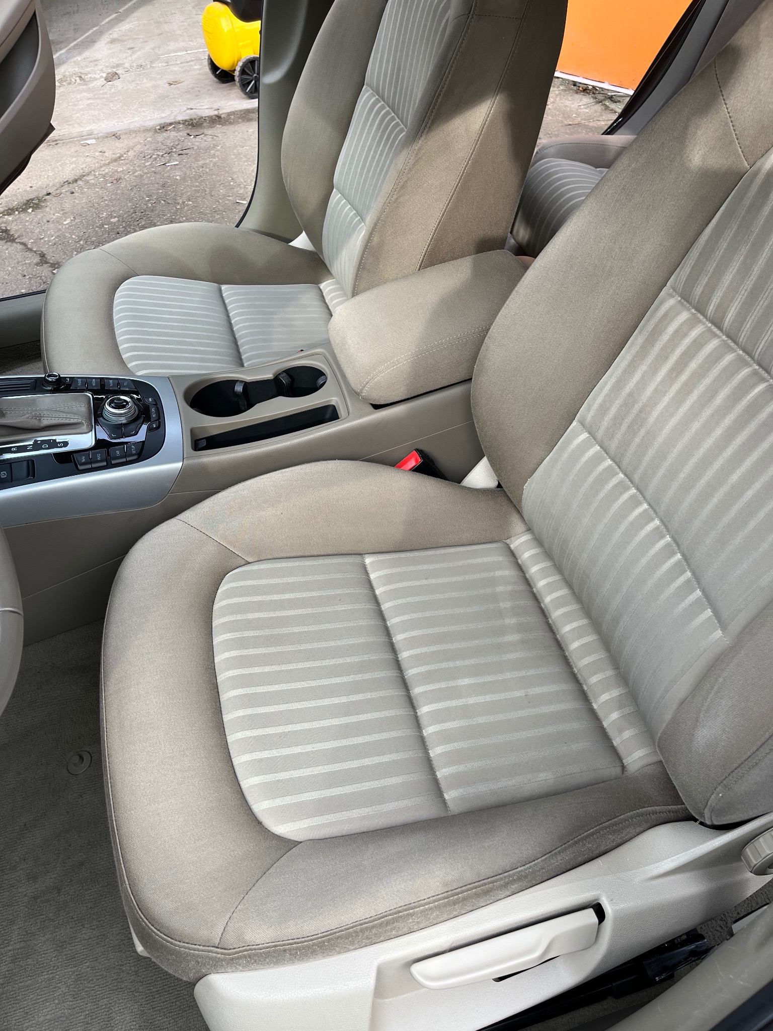 Beżowe fotele samochodowe z jasnymi paskami, widoczny panel sterowania i konsola środkowa z uchwytami na napoje.