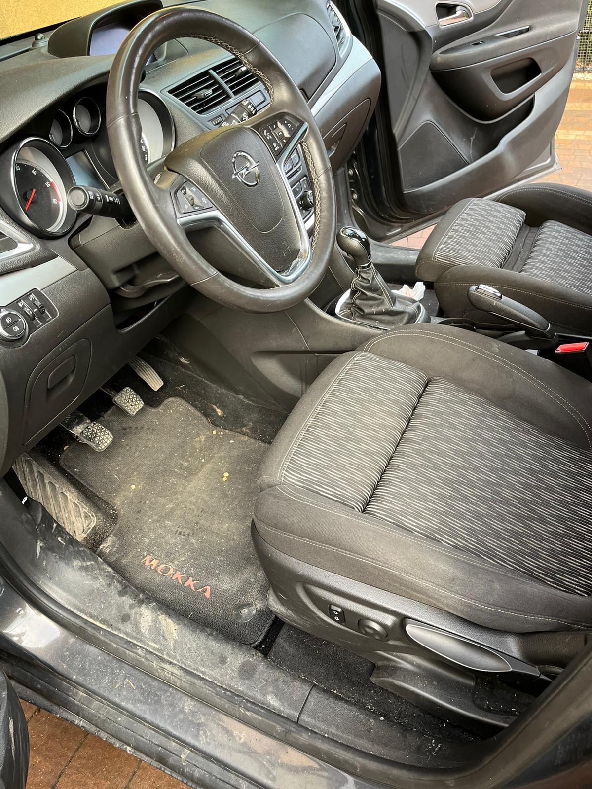 Wnętrze samochodu Opel Mokka z widocznymi, zabrudzonymi dywanikami i fotelami z tapicerką w paski.