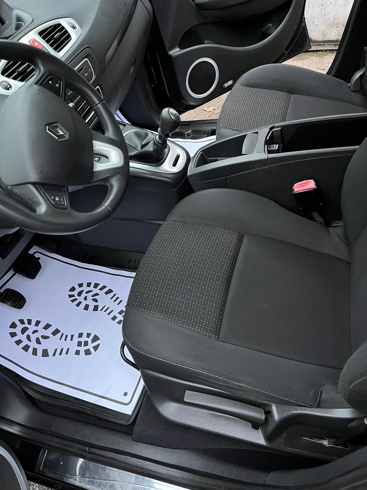 Wnętrze samochodu Renault z czarną tapicerką, widoczne fotele, kierownica, dźwignia zmiany biegów i ochronna mata podłogowa z nadrukowanymi śladami stóp.
