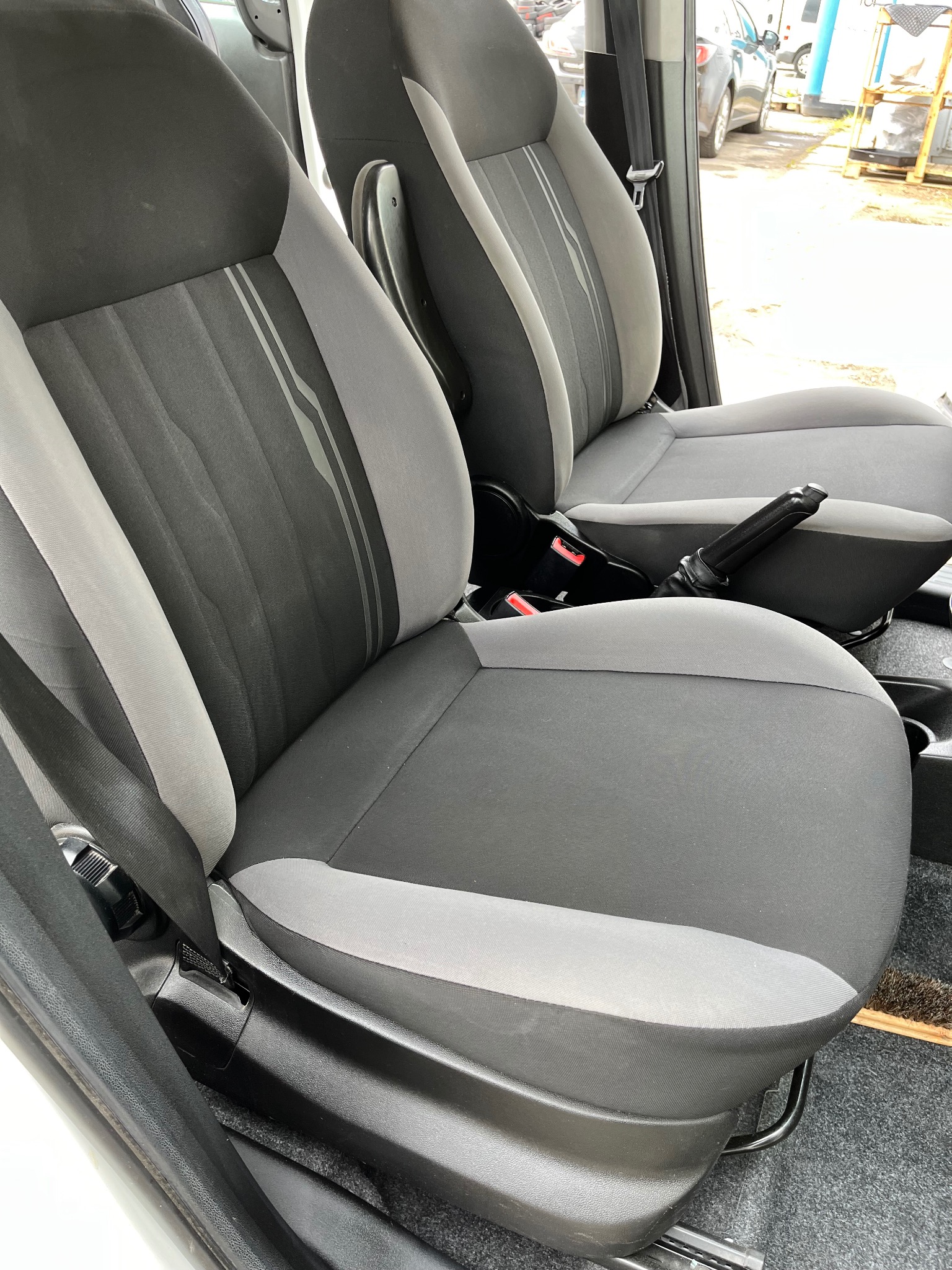 Dwa samochodowe fotele tapicerowane w odcieniach szarości z widocznymi pasami bezpieczeństwa i elementami regulacji, ukazujące detale faktury materiału i ergonomiczny kształt.