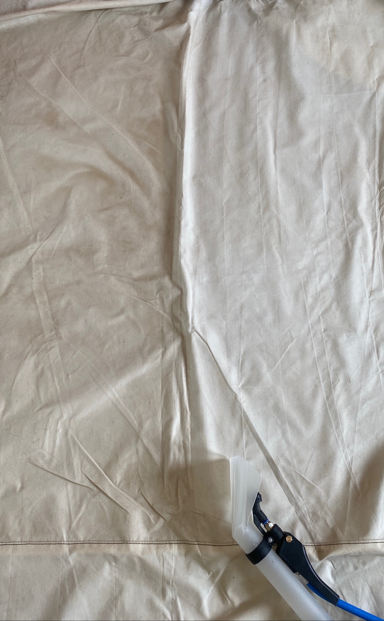 Fragment jasnej tkaniny z widoczną różnicą w czystości po użyciu urządzenia czyszczącego z przezroczystą ssawką i niebieskim przewodem.