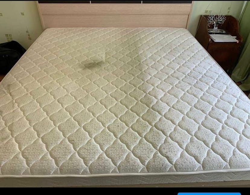 Duży materac z widocznymi plamami na powierzchni, umieszczony na ramie łóżka w sypialni.