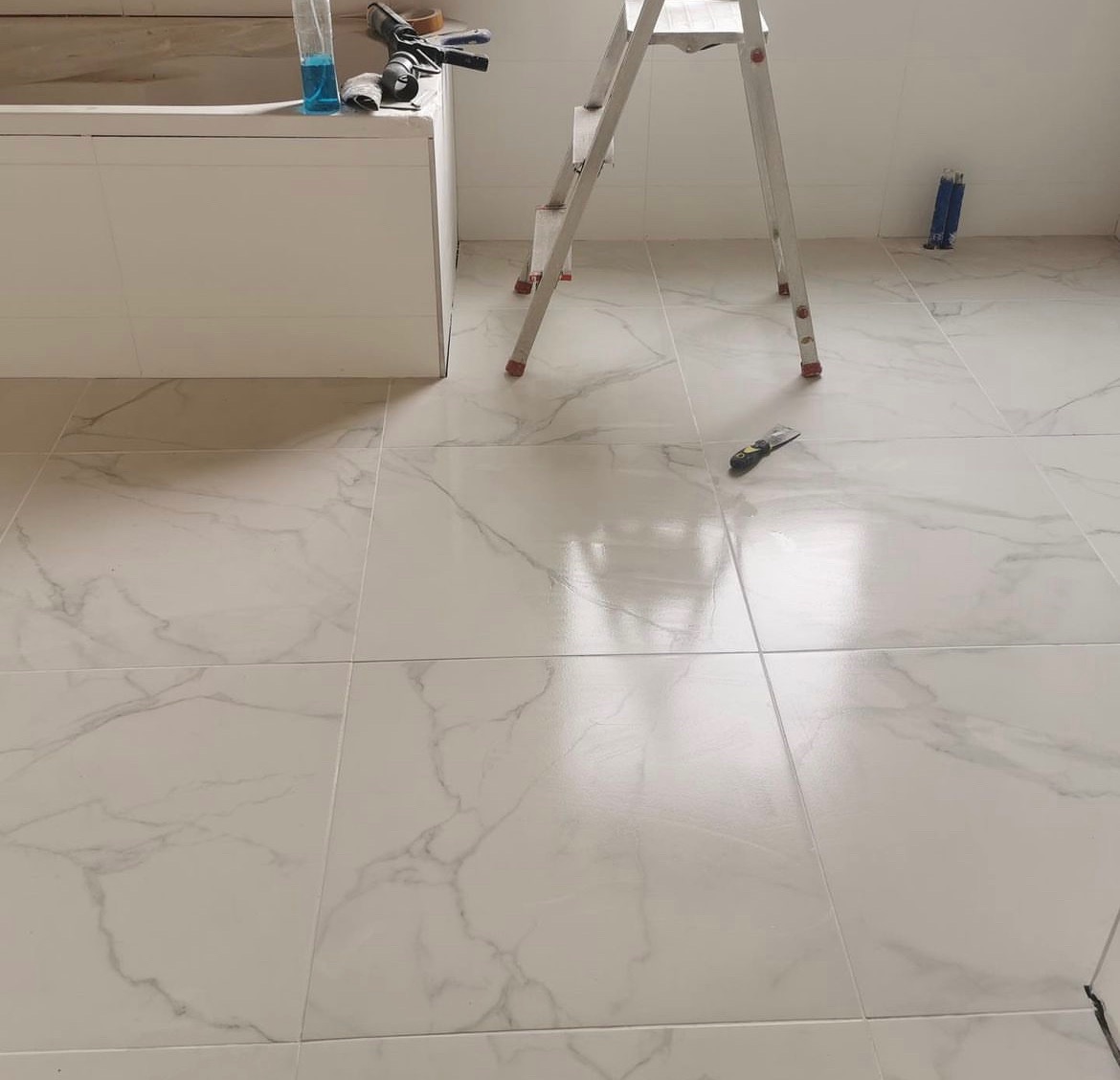 Świeżo położona, błyszcząca, biała marmurowa podłoga w łazience, z widocznymi narzędziami i drabiną, sugerującymi trwający remont.