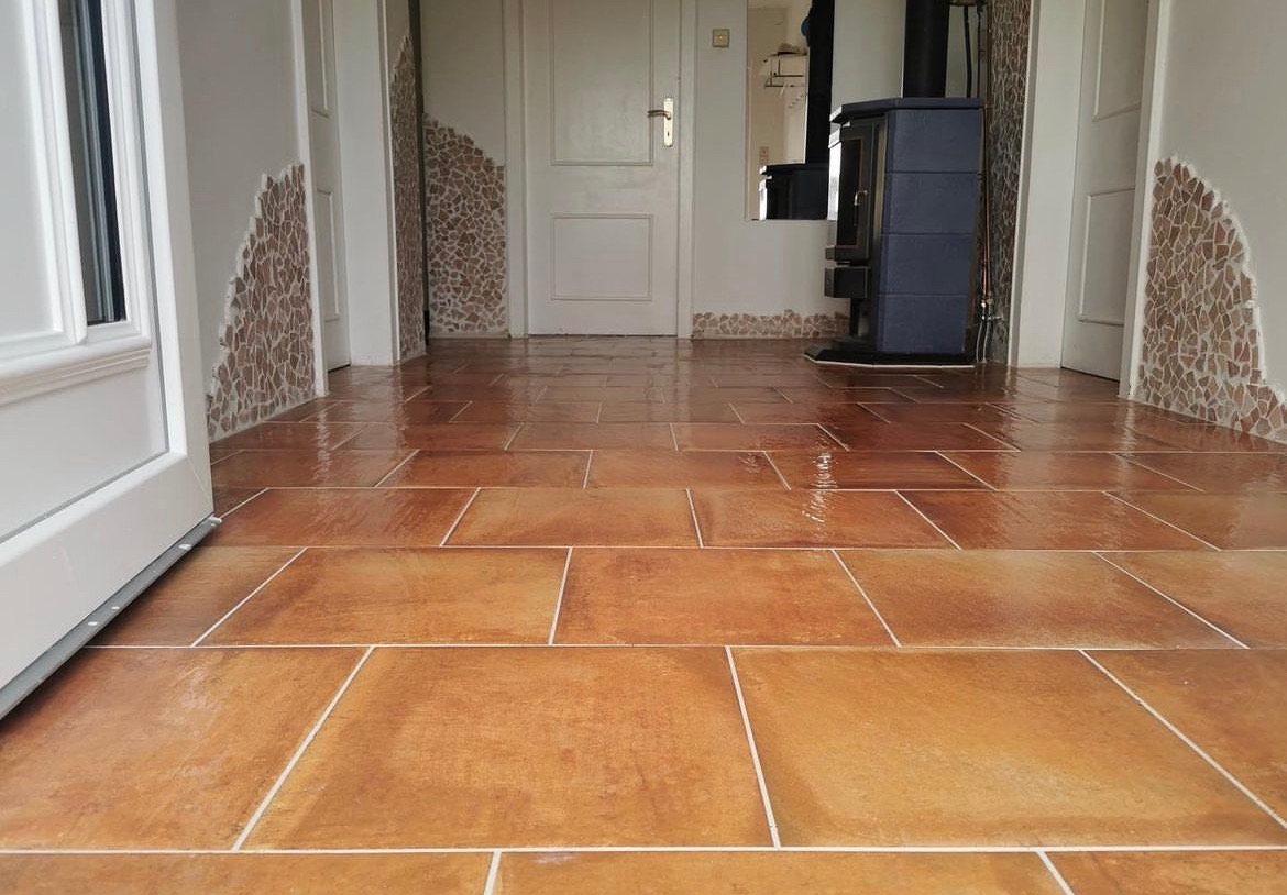 Błyszcząca, świeżo wyczyszczona terakota w korytarzu z dekoracyjnymi mozaikami na ścianach i piecem wolnostojącym w tle.