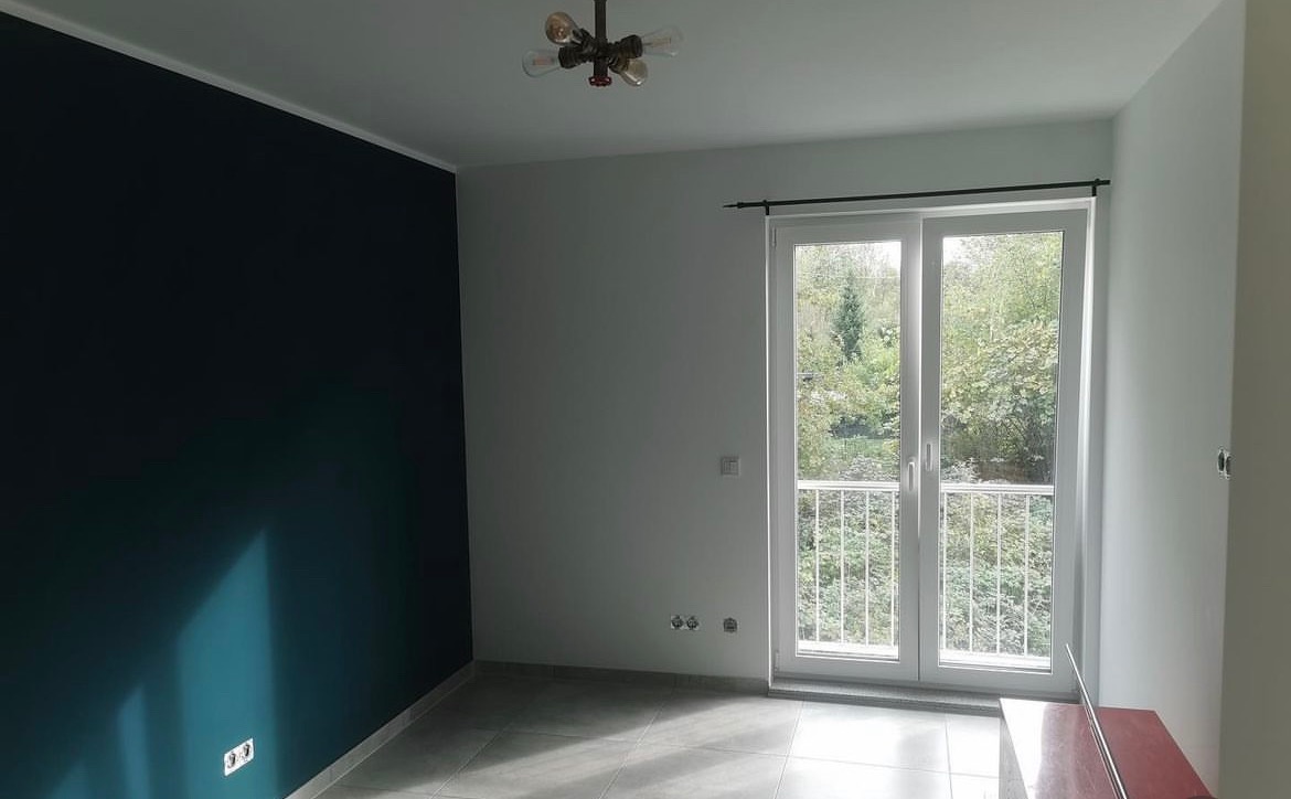 Pomalowane na granatowo ściana i szare płytki podłogowe w pokoju z balkonem i lampą sufitową w stylu retro.