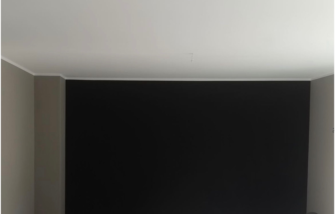 Pomalowana na czarno ściana z białym sufitem i listwą przypodłogową, widoczny fragment ściany bocznej w kolorze szarym, mały ubytek w rogu sufitu.