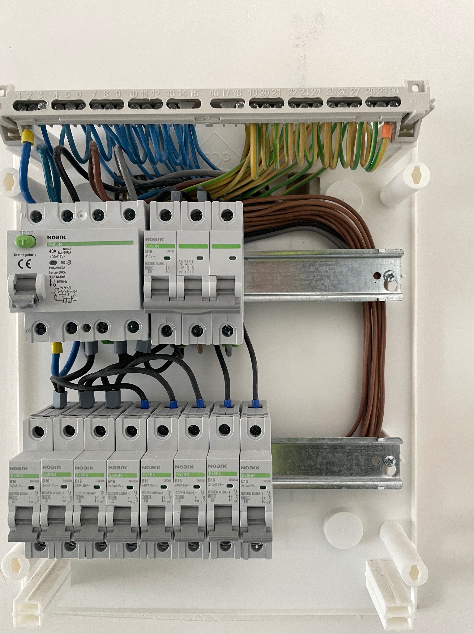 Rozdzielnica elektryczna z zamontowanymi bezpiecznikami Noark, widoczne przewody w różnych kolorach, szyny montażowe. Całość w białej obudowie.
