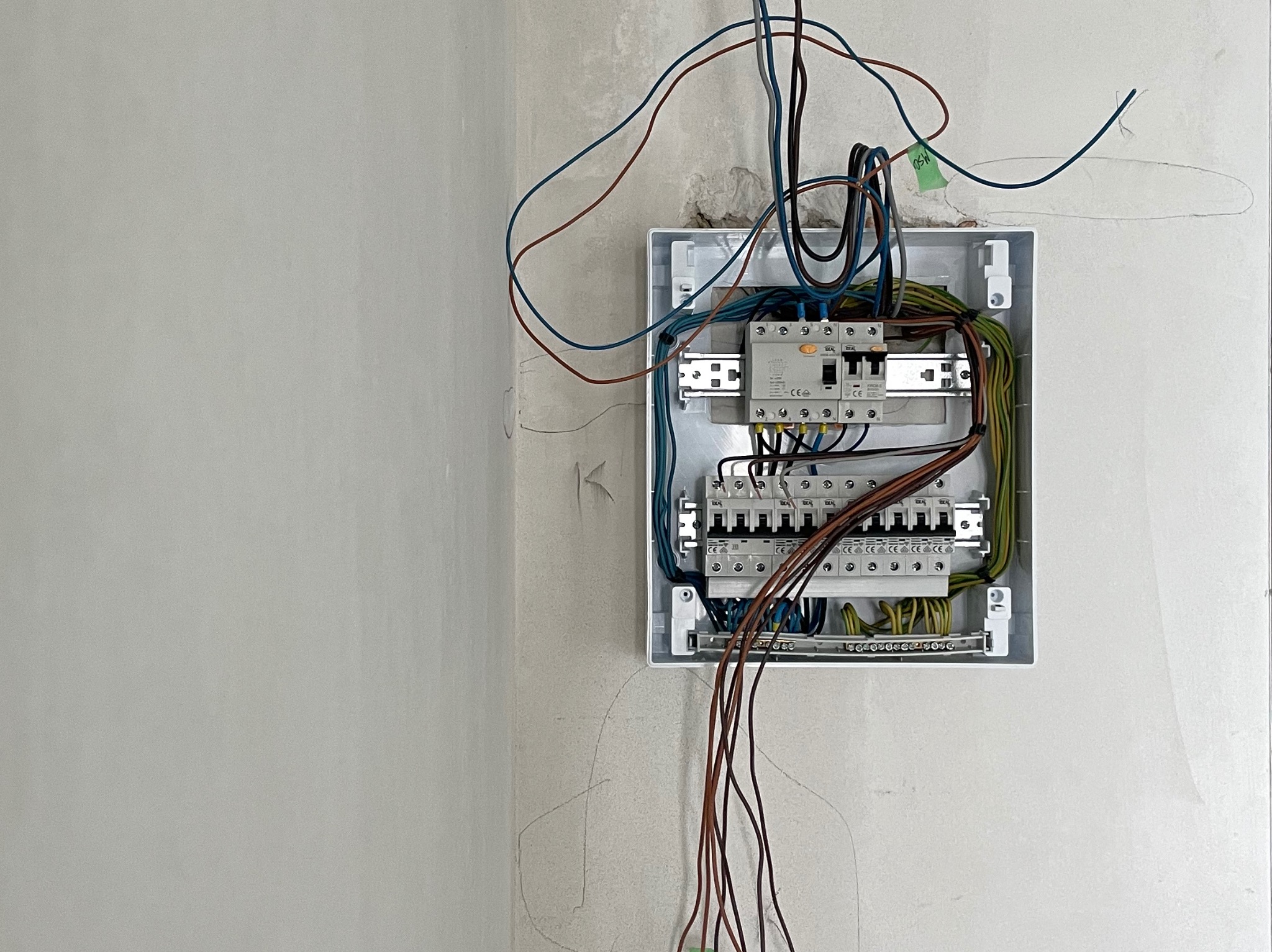 Rozdzielnica elektryczna z przewodami na surowej ścianie, widoczne zabezpieczenia i kable. Etap instalacji przed wykończeniem.