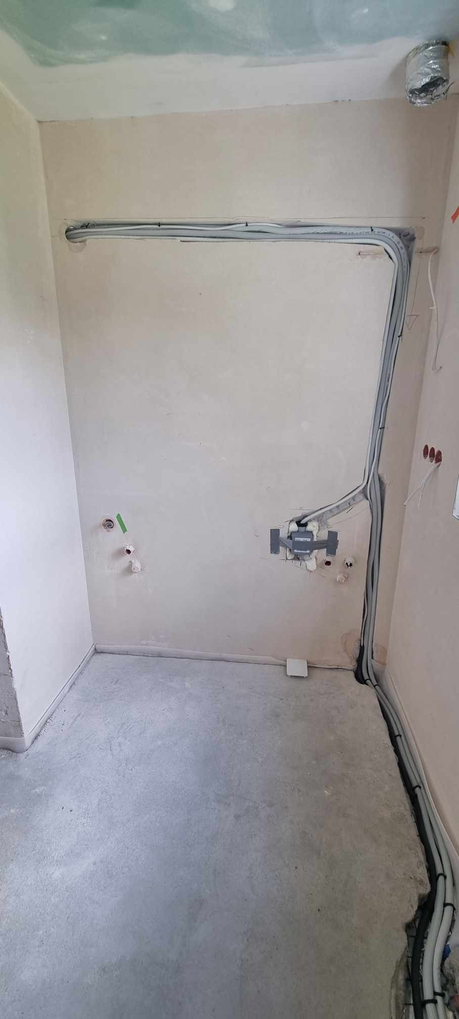 Wnętrze w trakcie remontu z widocznymi przewodami elektrycznymi ułożonymi wzdłuż ścian, przygotowane do montażu instalacji. Na suficie widoczny otwór wentylacyjny.