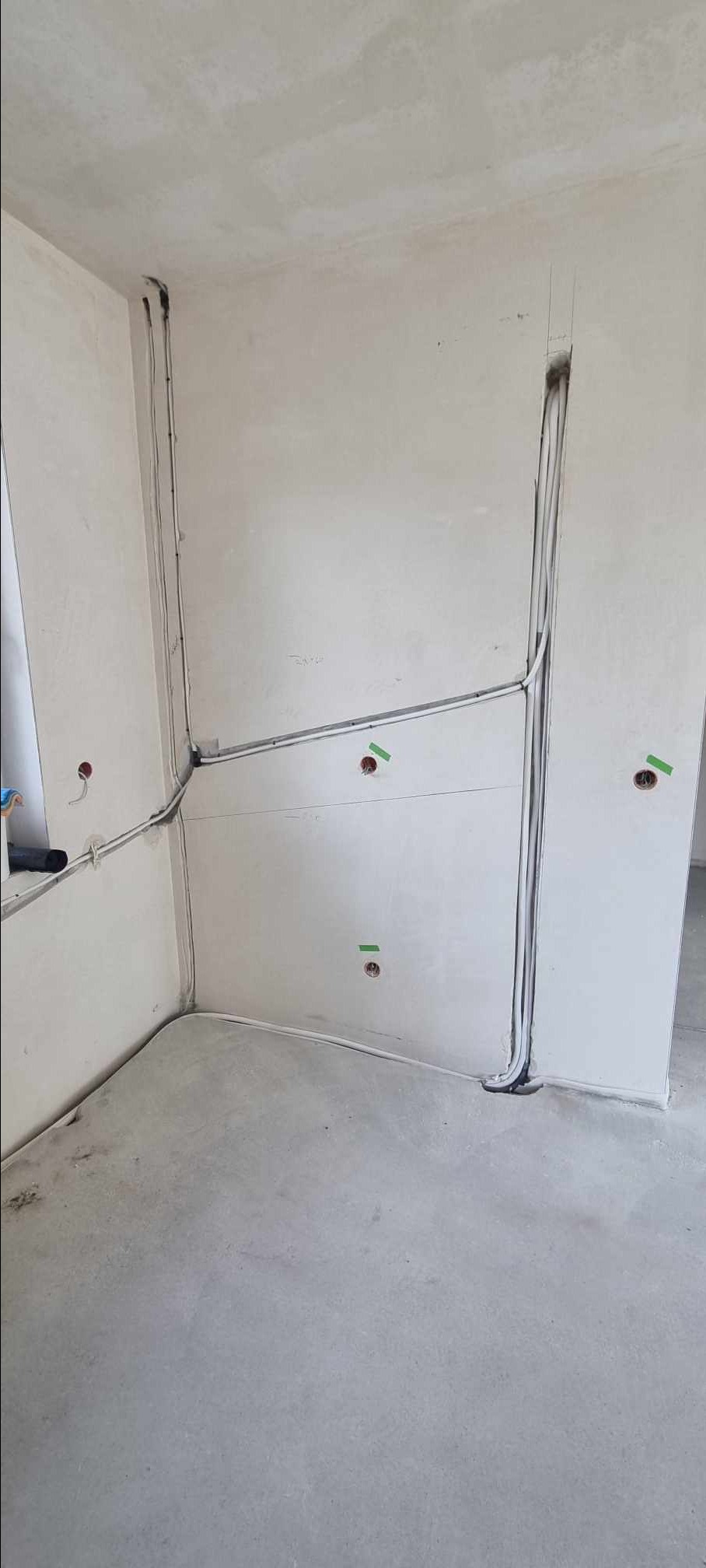 Surowy stan wykończenia wnętrza z widocznymi przewodami elektrycznymi prowadzonymi po ścianach i w bruzdach, przygotowanymi pod instalację.