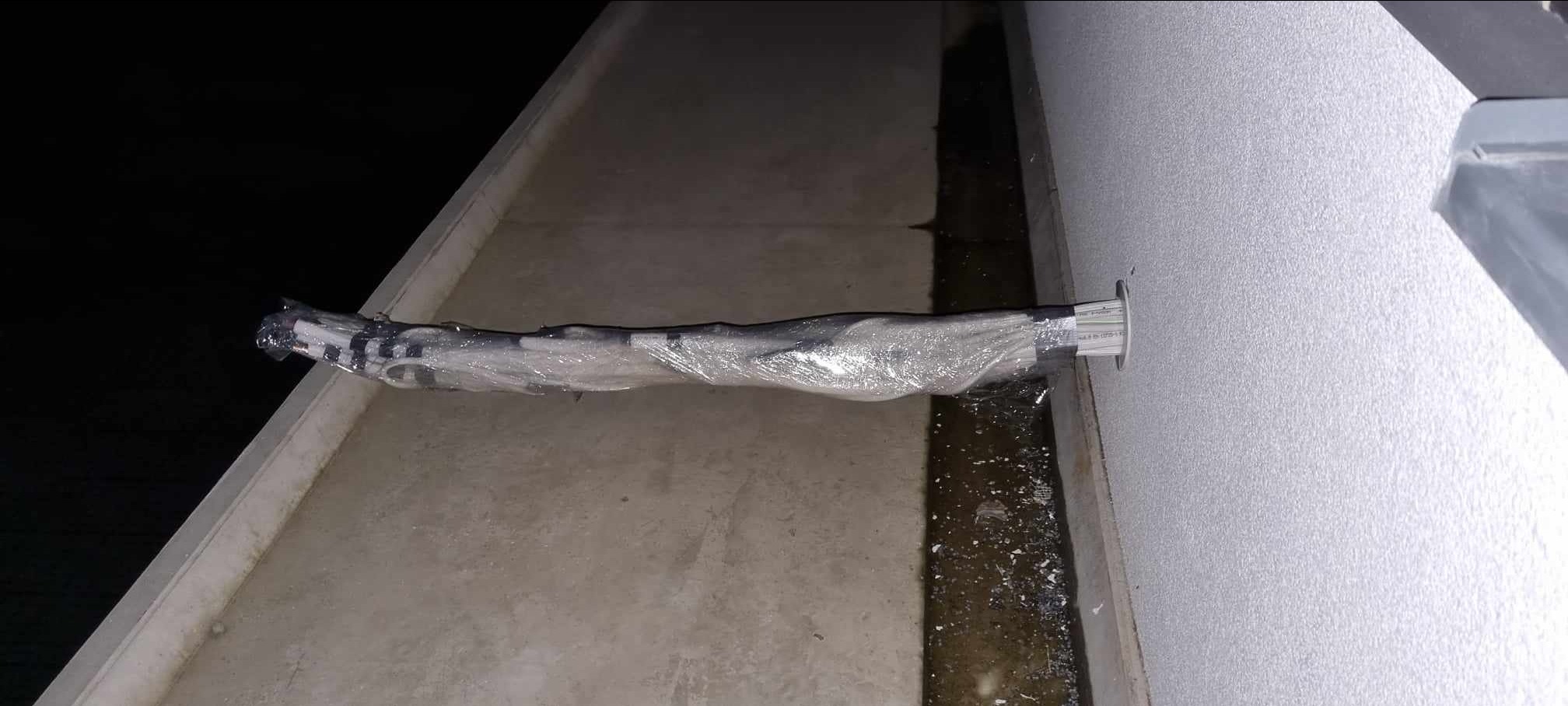 Rury w izolacji, prawdopodobnie do klimatyzacji, wystające ze ściany budynku w trakcie montażu, widoczne ślady wilgoci na podłożu.