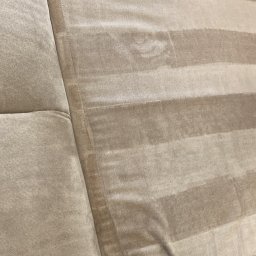 Pranie Tapicerki, konserwacja skór czyszczenie parowe, ozonowanie - Fragment sofy w beżowe pasy, widoczna różnica w kolorze po praniu ekstrakcyjnym, dysza odkurzacza piorącego w prawym dolnym rogu.