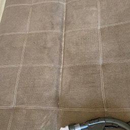 Pranie Tapicerki, konserwacja skór czyszczenie parowe, ozonowanie - Brązowa kanapa z widocznym efektem czyszczenia tapicerki; fragment wyczyszczony, widoczna dysza odkurzacza piorącego, plama na siedzisku i dziura w szwie.