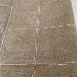 Pranie Tapicerki, konserwacja skór czyszczenie parowe, ozonowanie - Fragment brązowej kanapy z wyraźnymi przeszyciami, widoczne plamy i zabrudzenia na powierzchni materiału.