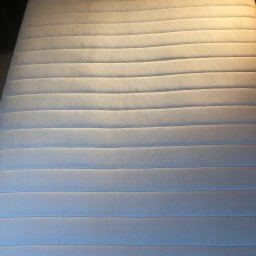 Pranie Tapicerki, konserwacja skór czyszczenie parowe, ozonowanie - Czysty, biały materac z poziomymi przeszyciami w regularnych odstępach, oświetlony z góry, ukazujący strukturę materiału i dbałość o detale.