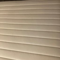 Pranie Tapicerki, konserwacja skór czyszczenie parowe, ozonowanie - Jasny, prążkowany materac z delikatnymi wgłębieniami, ukazujący czystą powierzchnię i regularny wzór. Widoczny fragment ciemnego zagłówka.