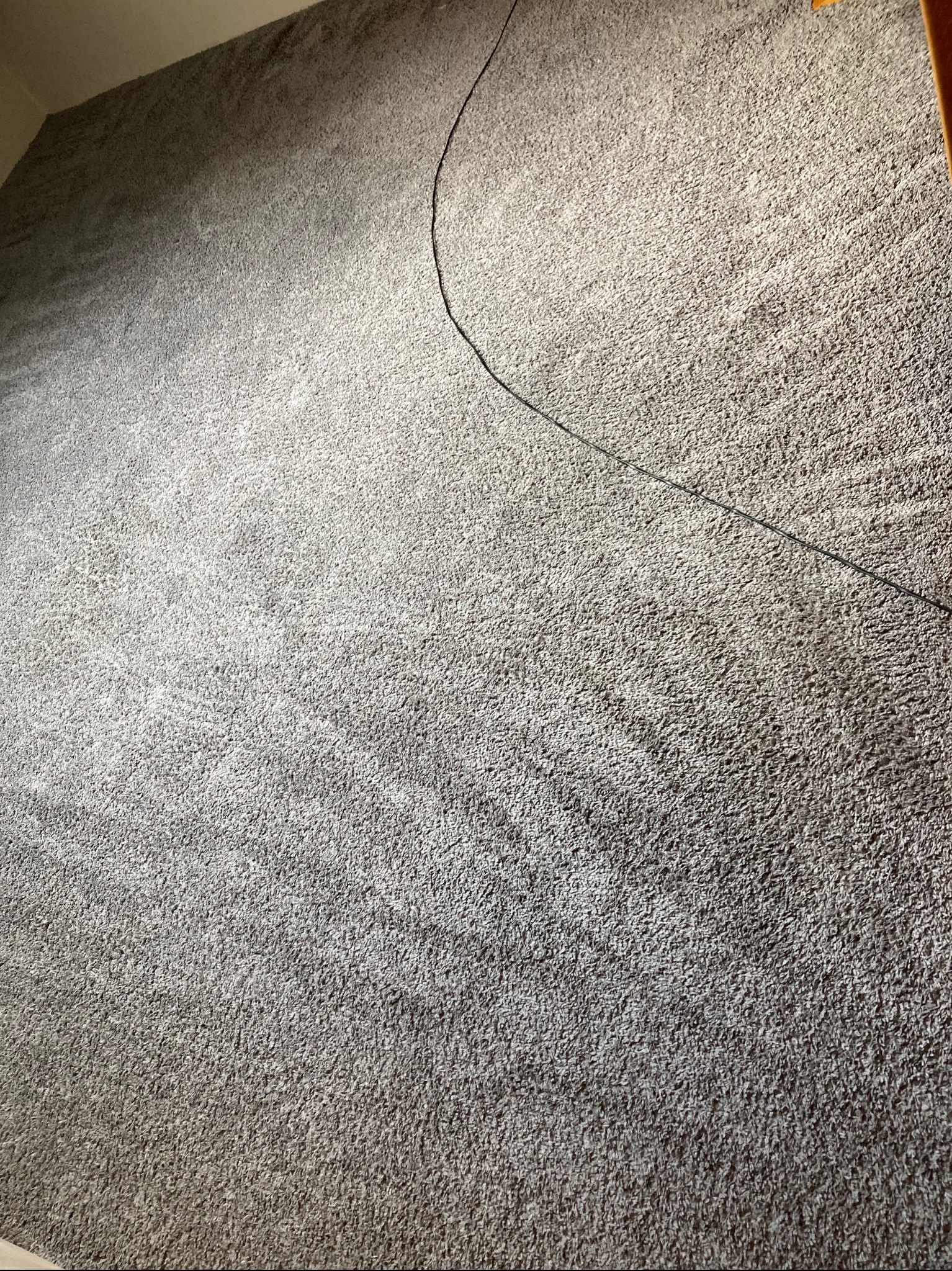 Szary, teksturowany dywan z widocznym śladem po czyszczeniu i leżącym kablem, ukazujący efekt po usłudze.