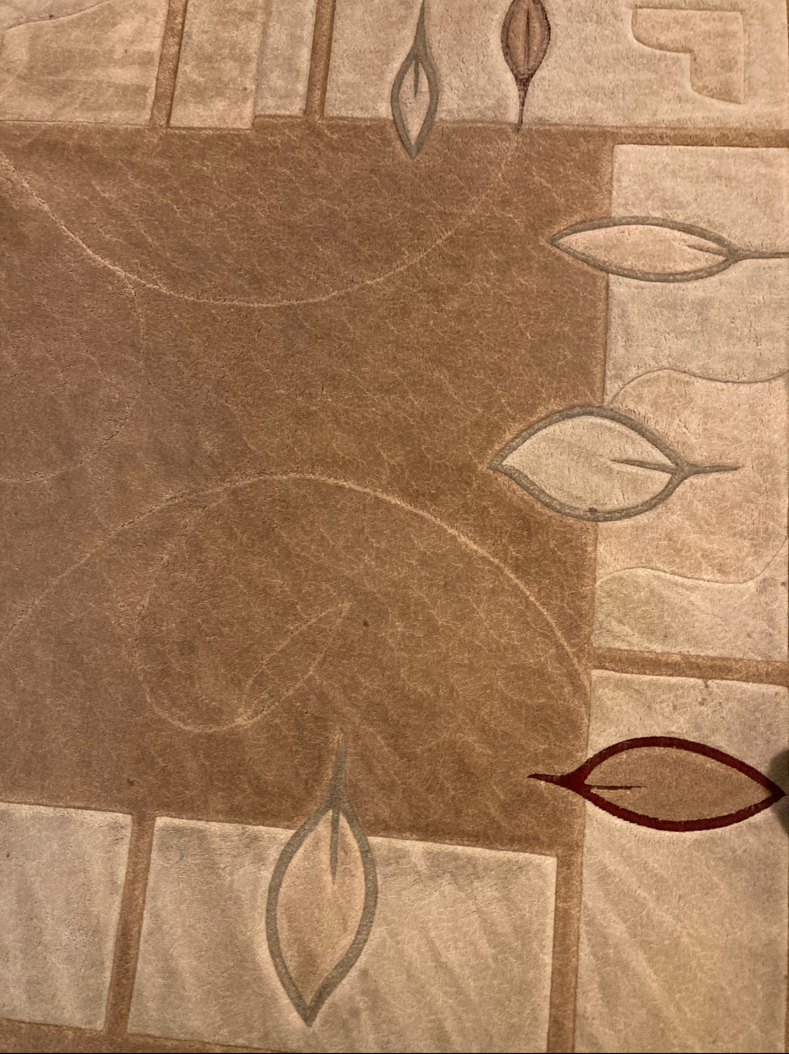 Wzór dywanu w odcieniach brązu i beżu z motywem liści, widoczne włókna i tekstura materiału. Regularny, geometryczny układ wzoru.