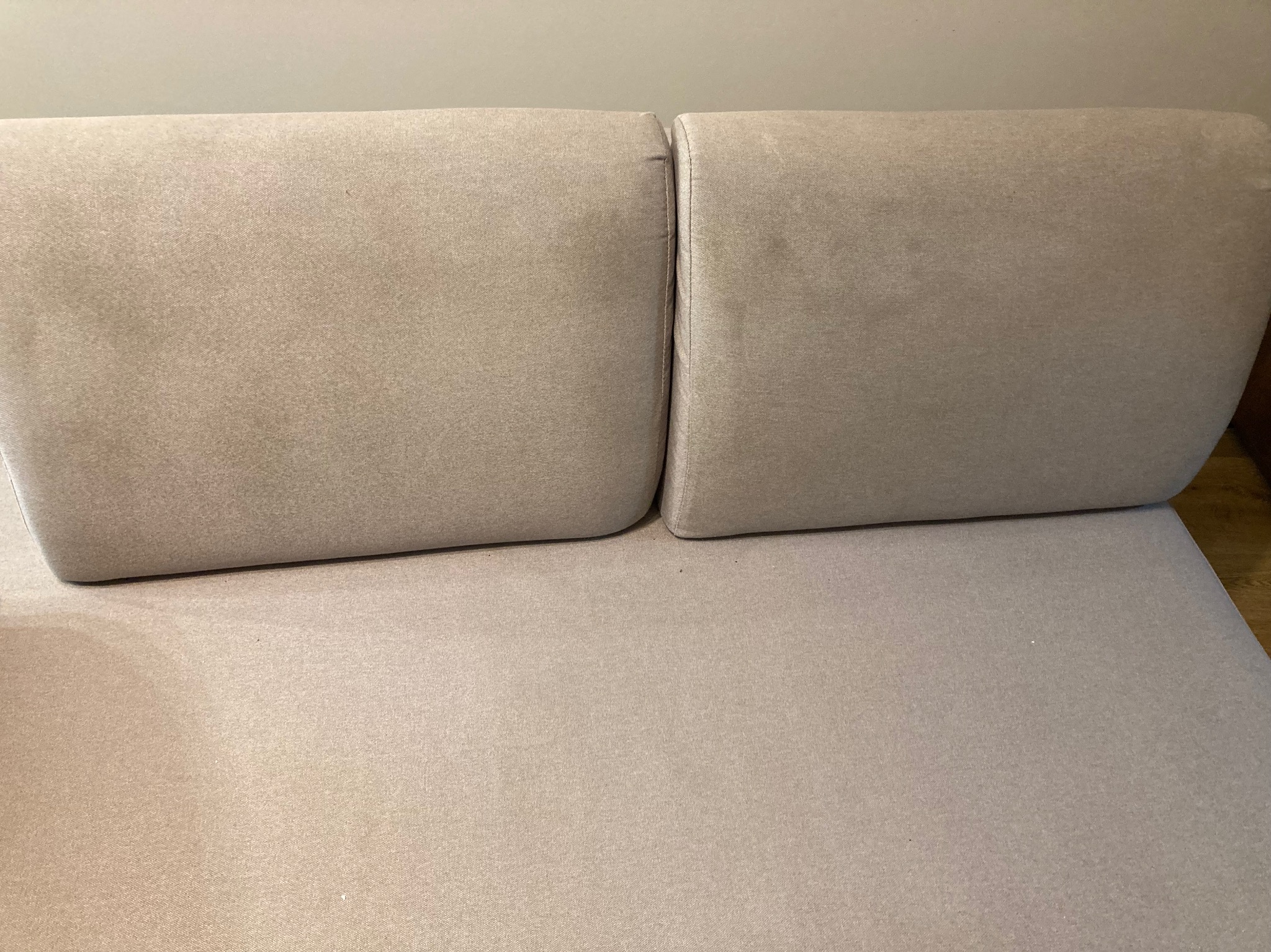Beżowa sofa z dwoma poduszkami o jednolitej teksturze materiału, widok z góry, bez wyraźnych plam lub zabrudzeń, sugeruje świeżo wypraną tapicerkę.