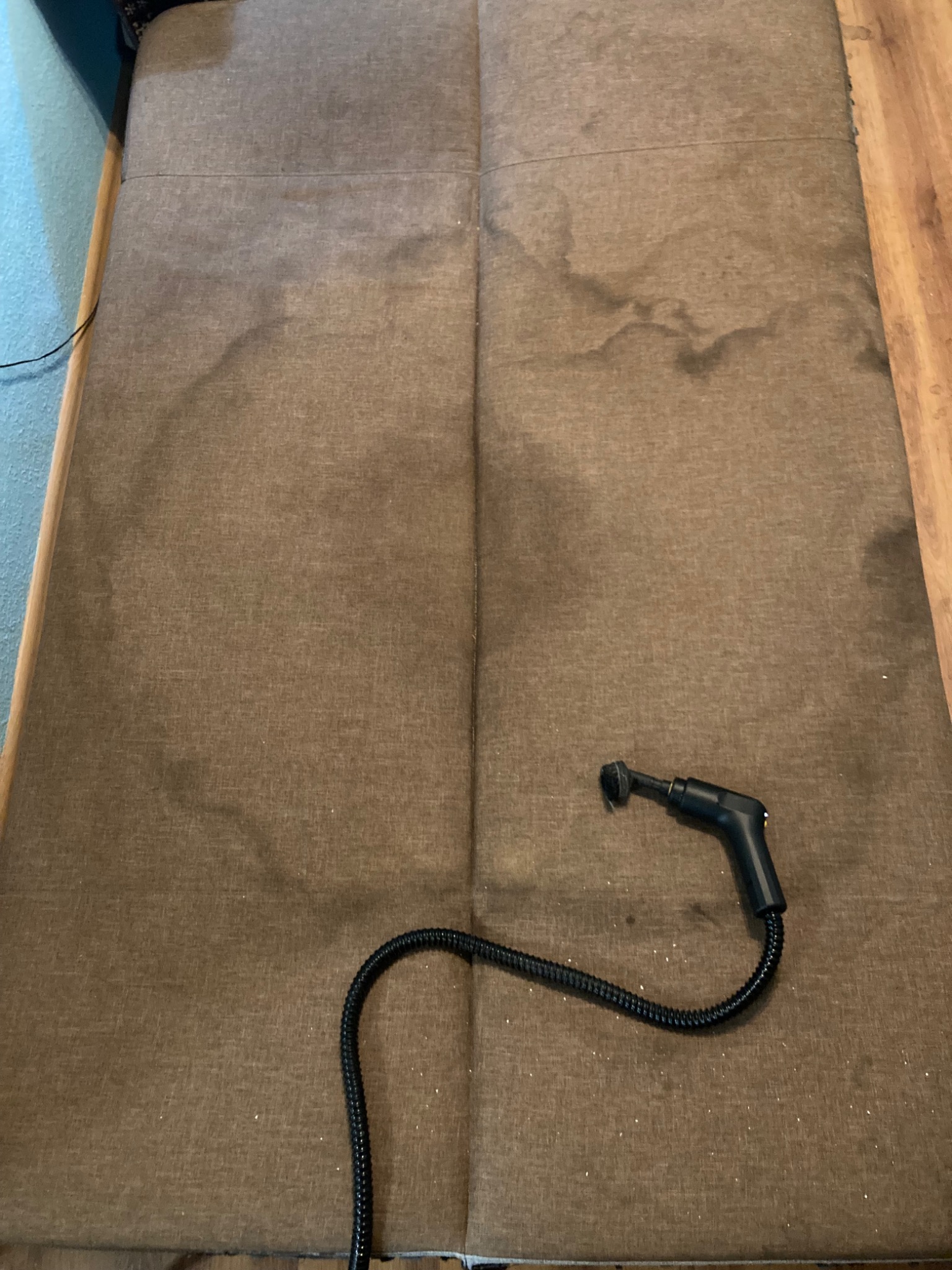 Brązowa kanapa z plamami i dyszą parową. Widoczne ślady czyszczenia tapicerki. Ujęcie z góry, podkreślające proces odświeżania i usuwania zabrudzeń.