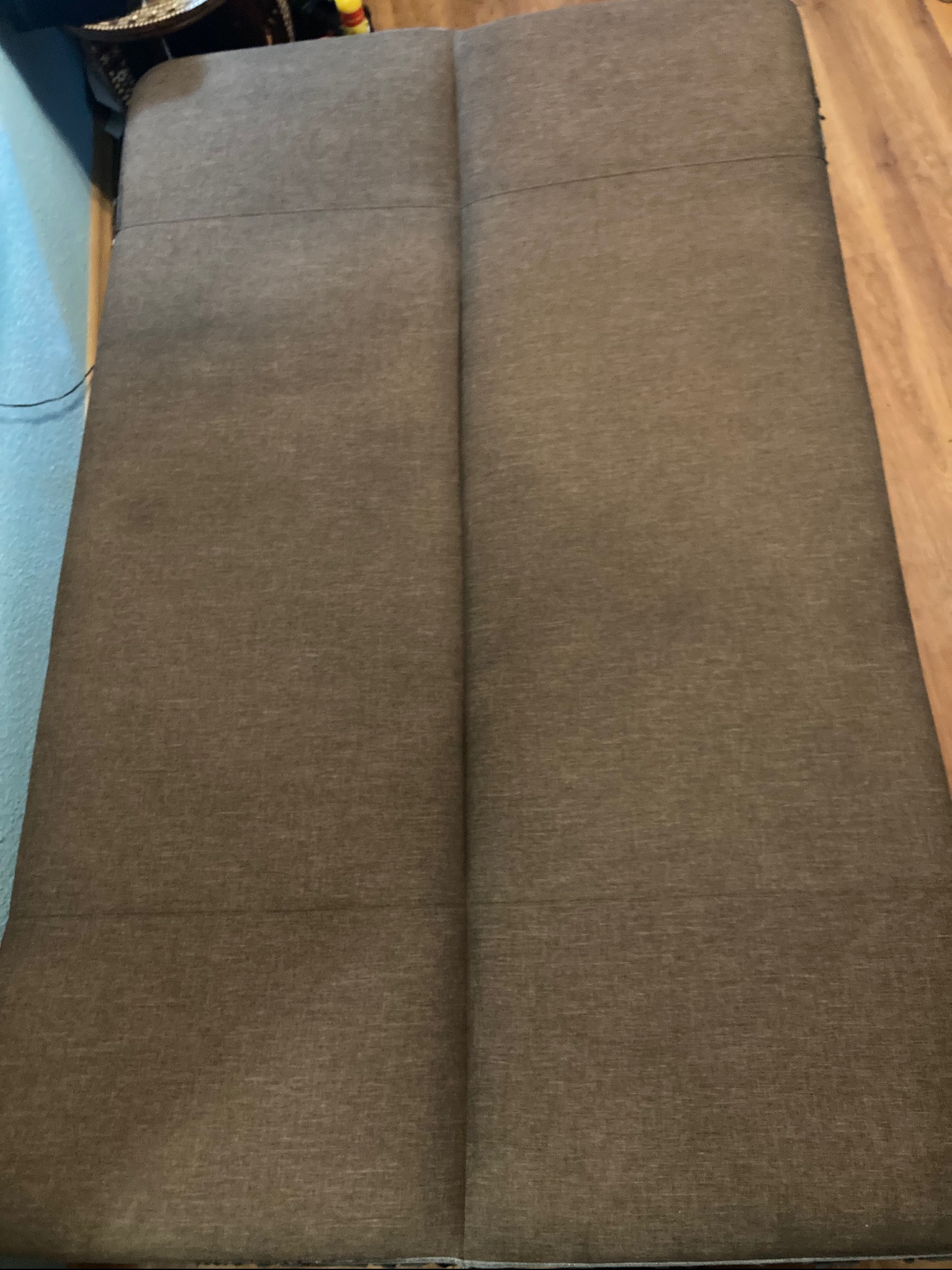 Brązowy, rozłożony materac na podłodze z paneli. Widoczna faktura tkaniny. Ujęcie z góry.