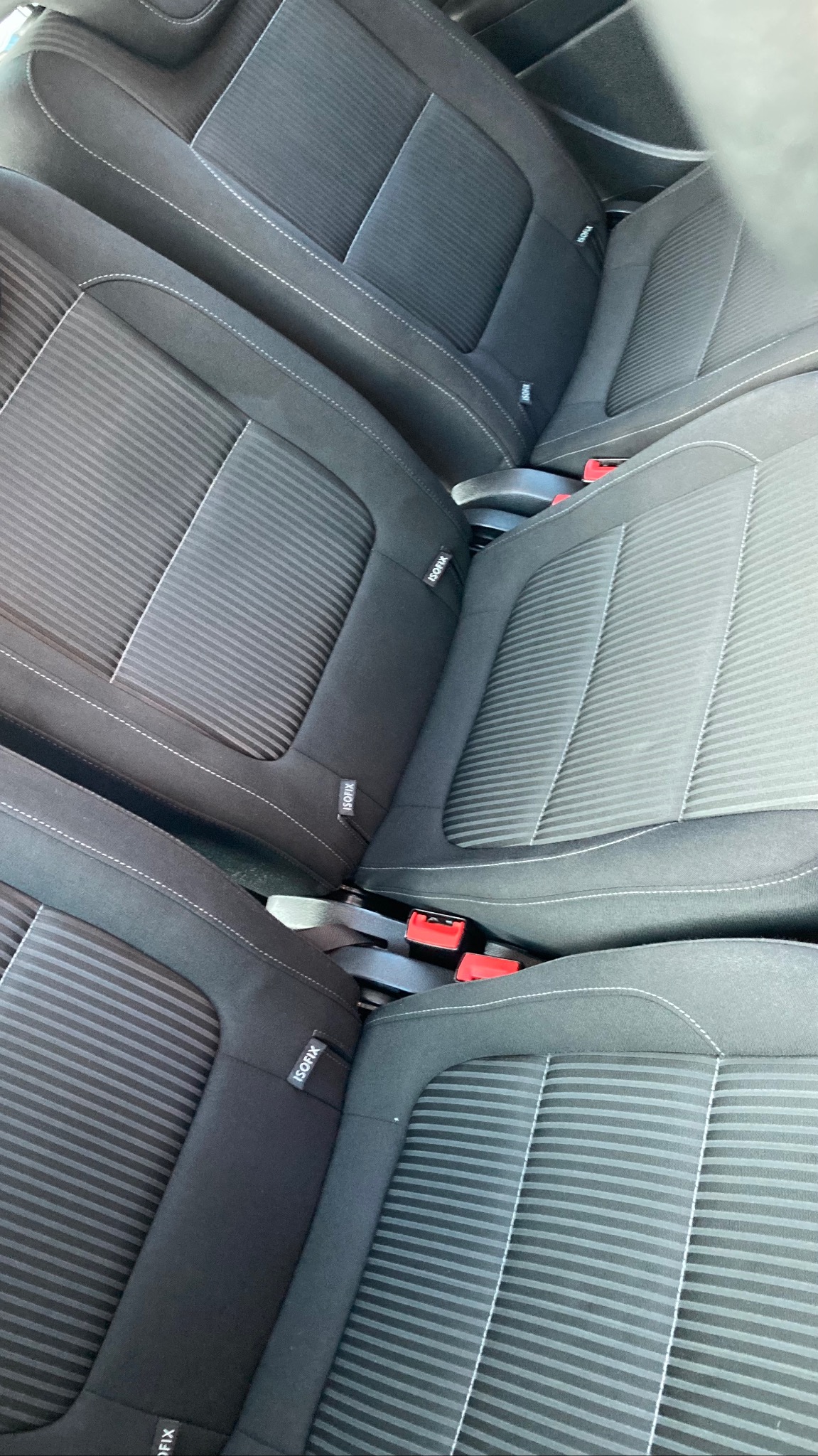 Czarne, tekstylne fotele samochodowe z systemem ISOFIX, widoczne z góry pod kątem. Delikatny wzór w paski i jasne szwy podkreślają detale tapicerki.