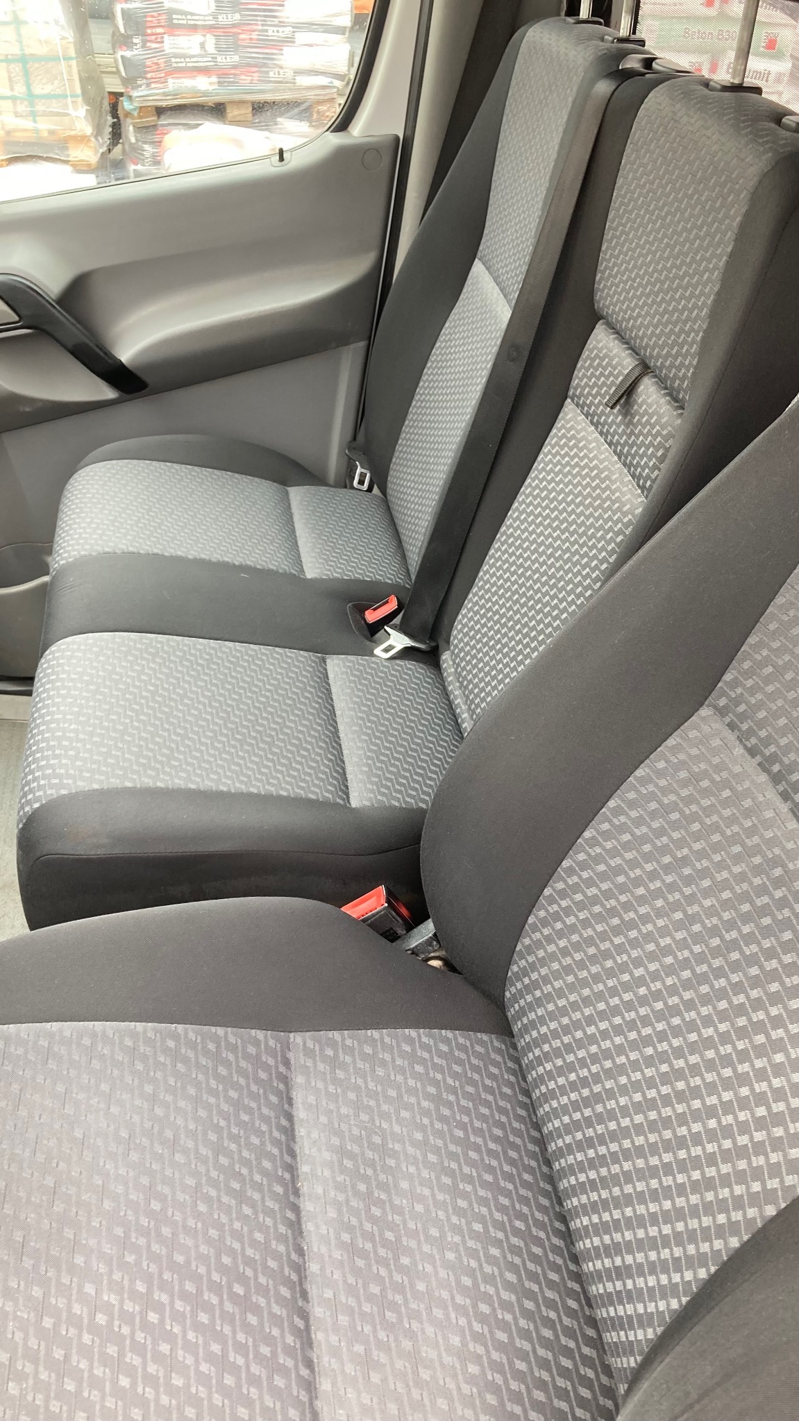 Szare fotele z tapicerką w geometryczny wzór wewnątrz pojazdu, widoczne pasy bezpieczeństwa i fragment deski rozdzielczej. Ujęcie z bliska, oświetlenie naturalne.