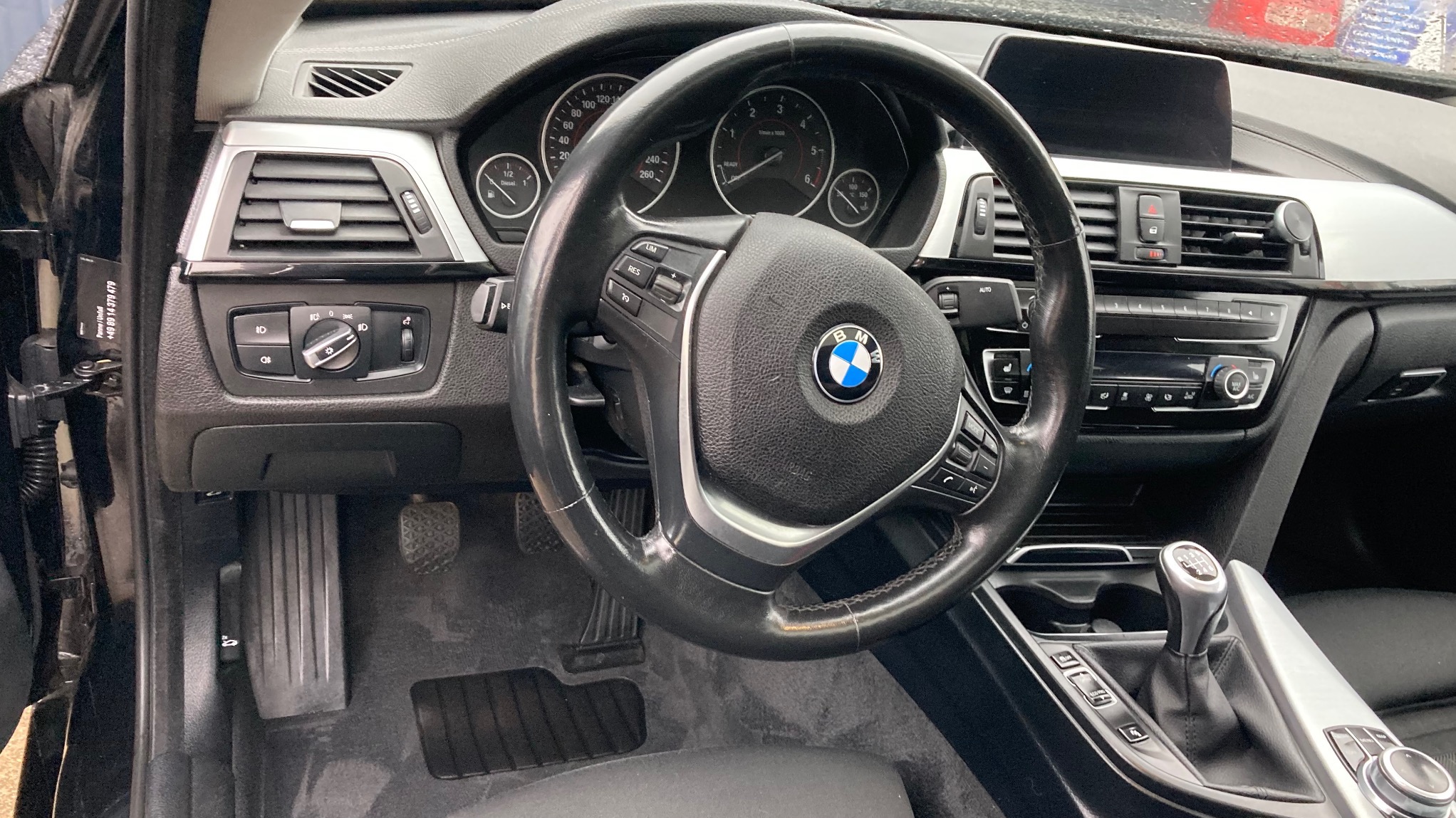 Wnętrze czarnego BMW serii 3: kierownica z logo, deska rozdzielcza z srebrnymi akcentami, czarna tapicerka podłogowa. Widok z perspektywy kierowcy.