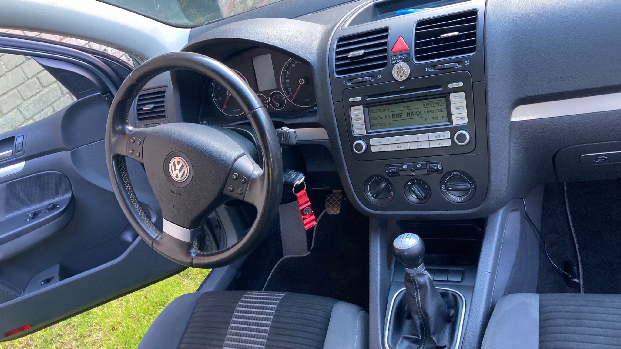 Wnętrze samochodu marki Volkswagen Golf V: deska rozdzielcza, kierownica, radio z wyświetlaczem, dźwignia zmiany biegów i częściowo widoczne siedzenia z wzorem w kratę.