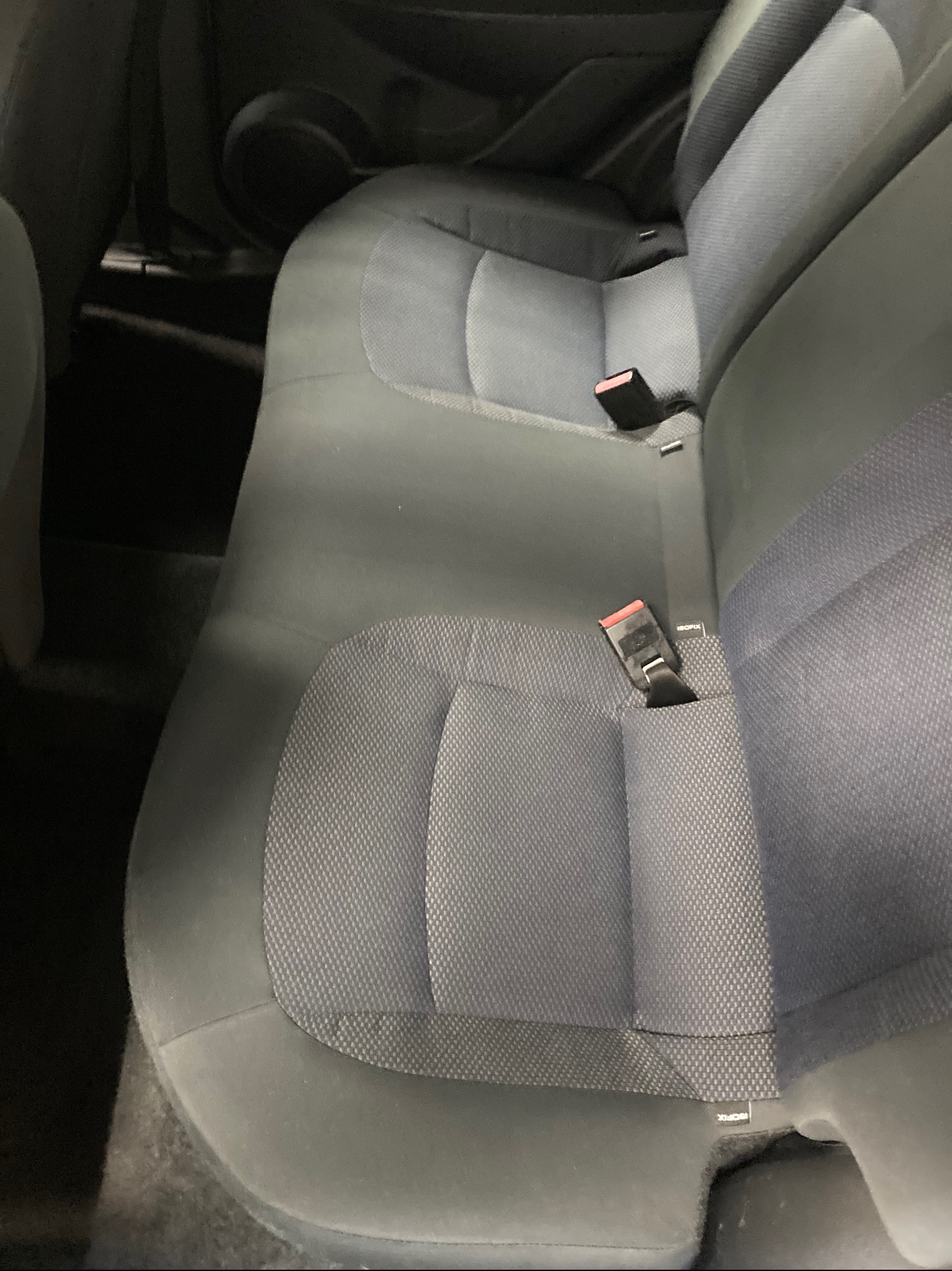 Szare, tekstylne siedzenie samochodowe z dwoma pasami bezpieczeństwa, widoczne mocowania ISOFIX. Ujęcie z bliska, wnętrze pojazdu.