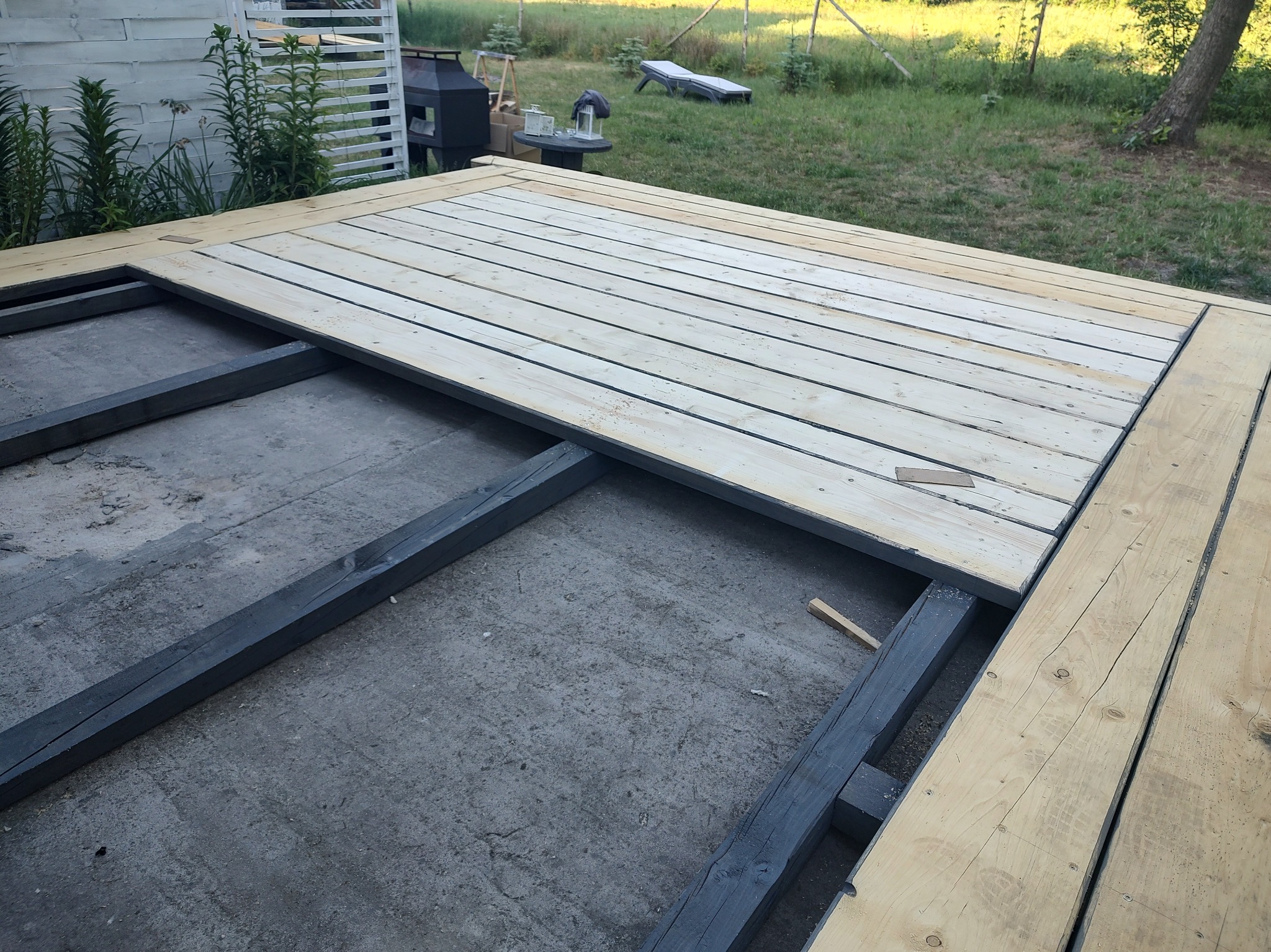 Budowa tarasu: widok na częściowo ułożoną drewnianą podłogę na czarnej, drewnianej konstrukcji ramy, w tle trawnik.