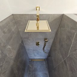 Marcin Tomaszewski Usługi Remontowe - Nowoczesny prysznic z szarymi płytkami imitującymi marmur, złotą armaturą i odpływem liniowym.