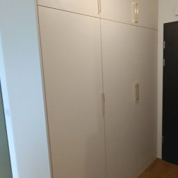 Kamil Żeliszczak - Wysoka, zabudowana szafa wnękowa z jasnymi, gładkimi frontami i minimalistycznymi, pionowymi uchwytami, dopasowana do skosu ściany w przedpokoju.