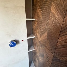 CatHouse - Nowoczesna łazienka z drewnianą ścianą w jodełkę, jasnymi płytkami i wnęką z półkami. Widoczny element armatury. Minimalistyczny design.