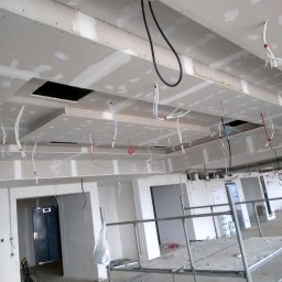 CatHouse - Sufit podwieszany z płyt gipsowo-kartonowych w trakcie montażu, widoczne kable i otwory, rusztowanie w tle. Prace wykończeniowe w nowym budynku.