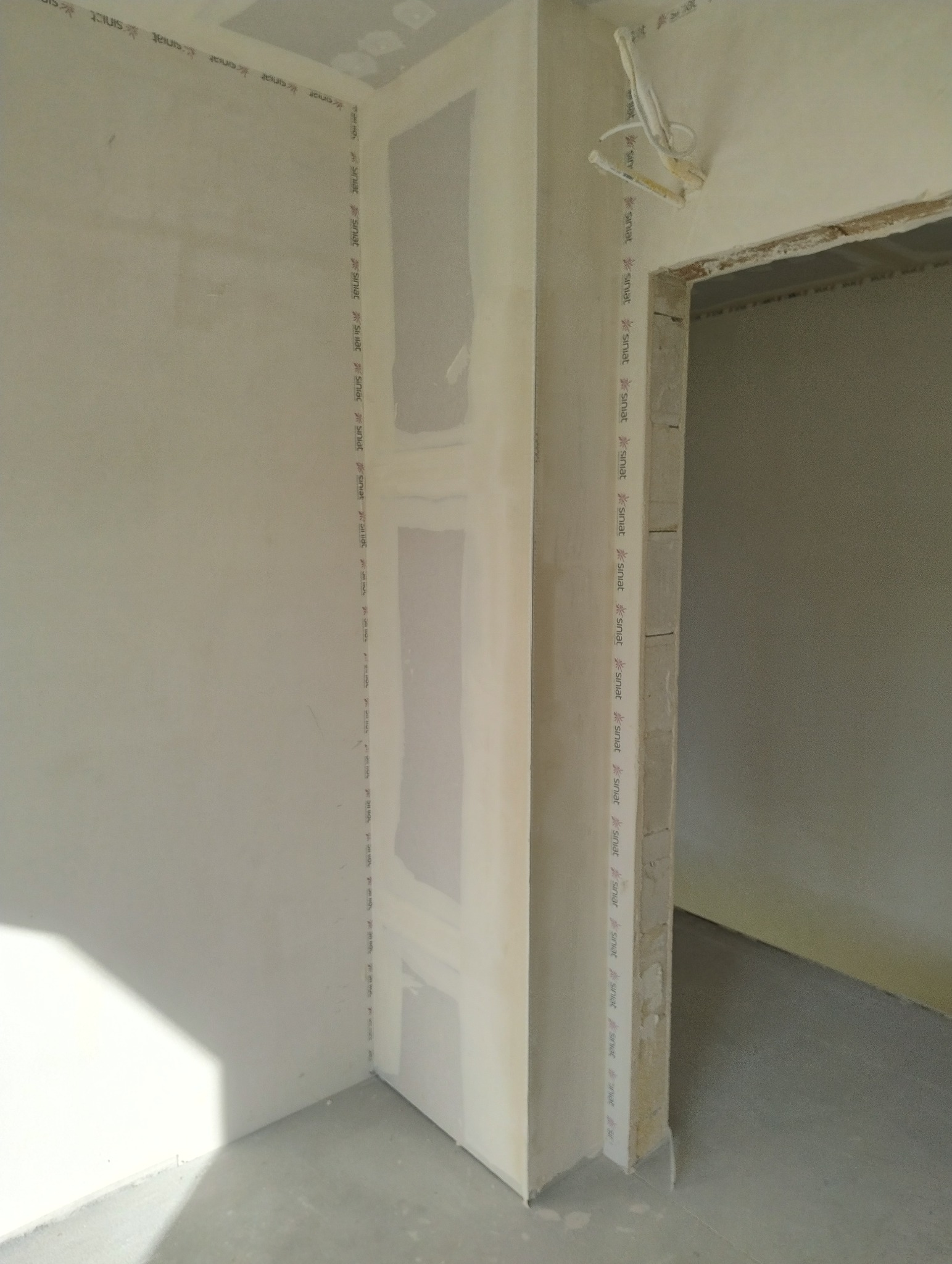 Montaż płyt karton-gips na ścianie, widoczne profile i łączenia. Świeże, surowe wykończenie wnętrza w trakcie prac. Fragment instalacji elektrycznej przy futrynie.