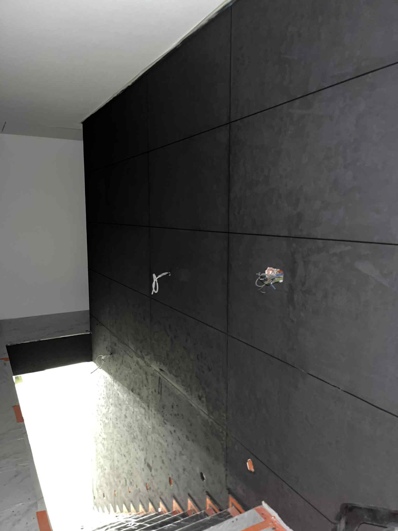 Ciemnoszara ściana wykończona płytami, widoczne kable elektryczne i fragment schodów. Ujęcie z dołu, podkreślające strukturę i detale wykończenia wnętrza.