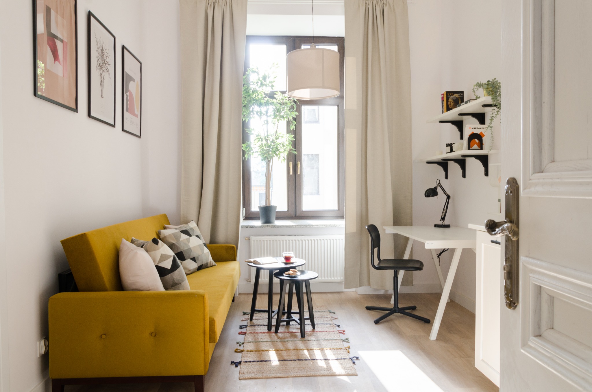 Jasne wnętrze mieszkania w Łodzi z żółtą sofą, biurkiem do pracy i dekoracjami, oświetlone naturalnym światłem wpadającym przez okno.