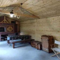 Wnętrze altany z drewnianą boazerią, ceglanym grillem z piecem chlebowym, drewnianymi skrzyniami i reżyserskim krzesłem.